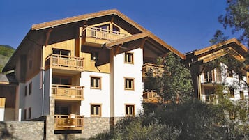 A multi-story building with balconies, stone foundation, and a mountainous backdrop.