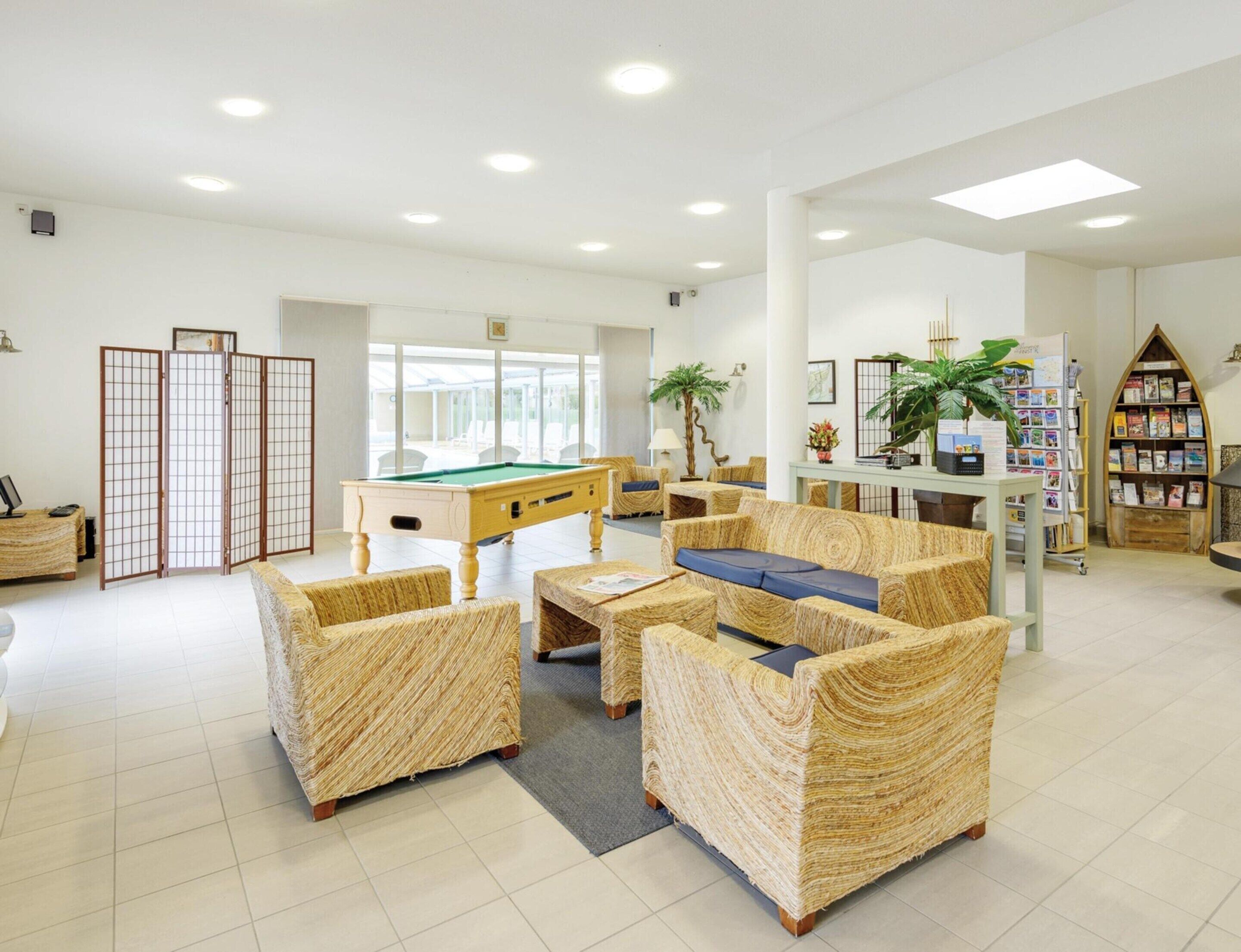 A spacious indoor area with a pool table, wicker furniture, and a bookshelf.