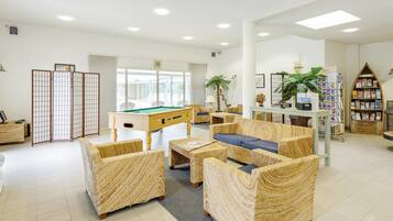 A spacious indoor area with a pool table, wicker furniture, and a bookshelf.