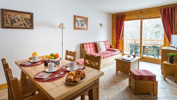 A cozy room with a wooden table set for breakfast, a sofa with a plaid blanket, and a window with curtains.