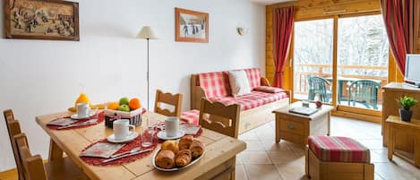 A cozy room with a wooden table set for breakfast, a sofa with a plaid blanket, and a window with curtains.