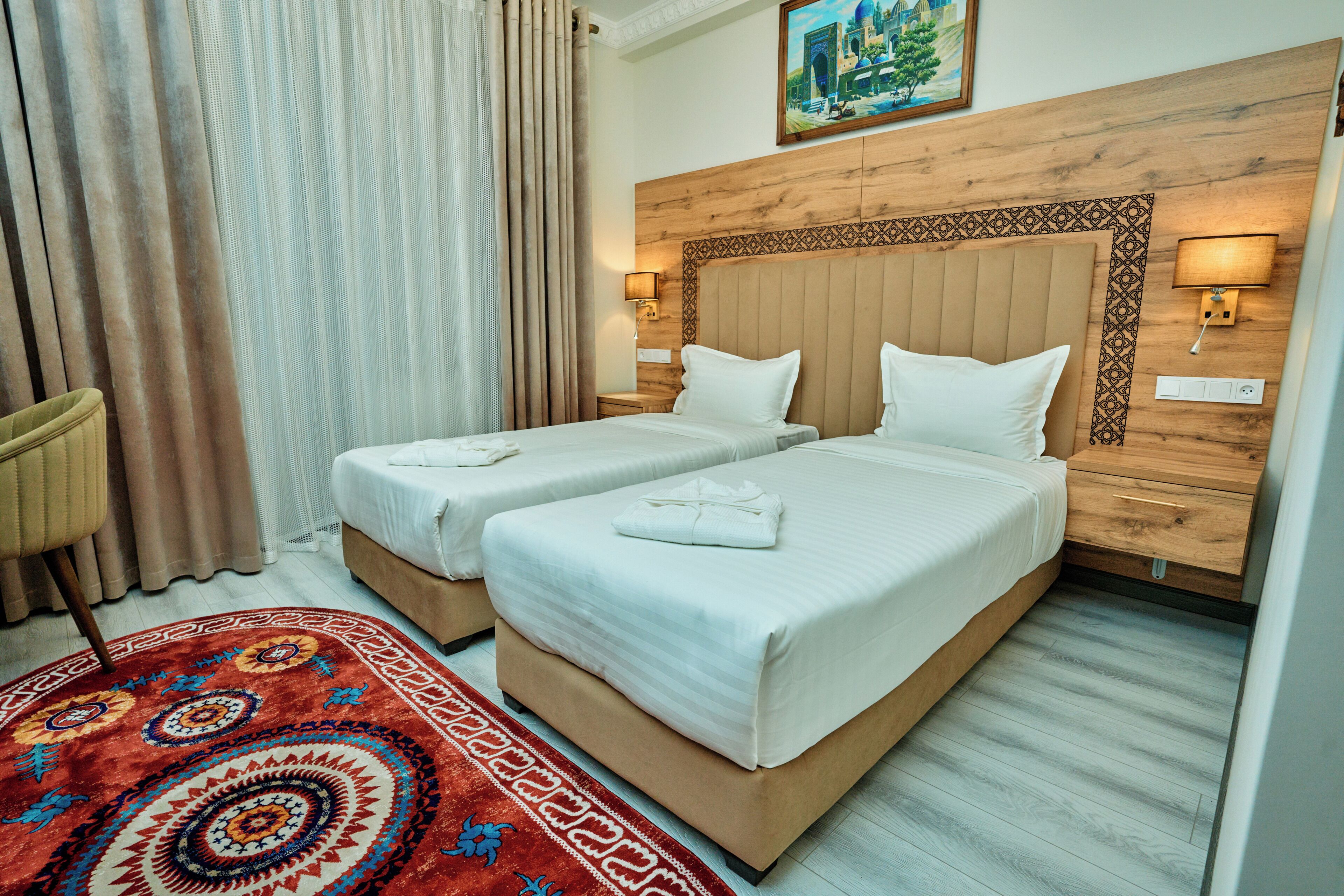 Quarto de hotel com duas camas, uma cabeceira de madeira, um tapete estampado e um quadro na parede.
