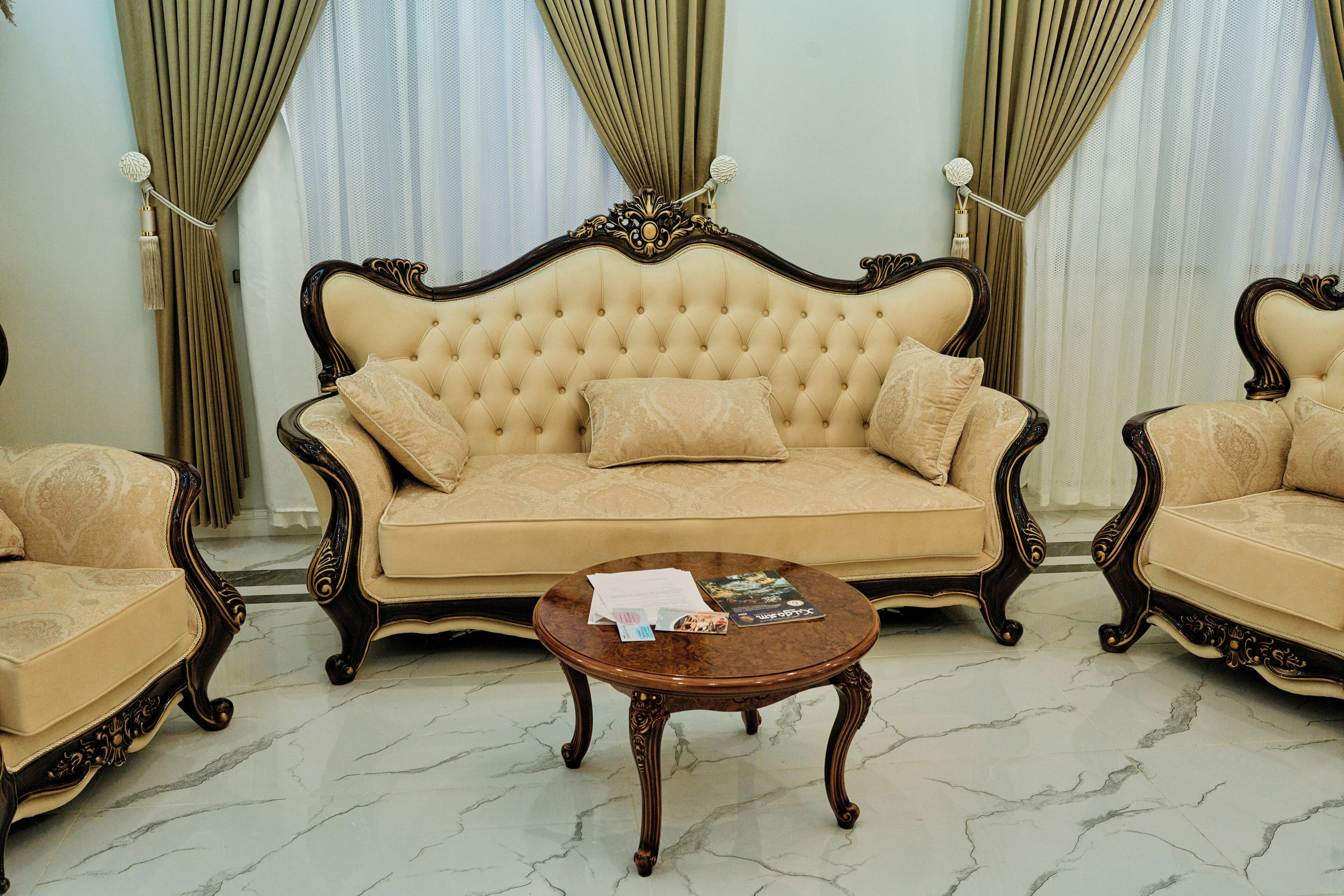 Um quarto com sofá estofado, poltronas a combinar e piso de mármore.