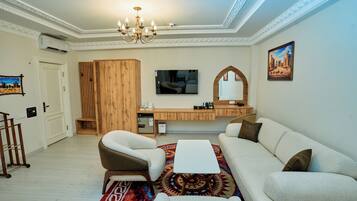 Ein Wohnzimmer mit einer Couch, Sesseln, einem Couchtisch, einem Fernseher und einer Holzkommode.