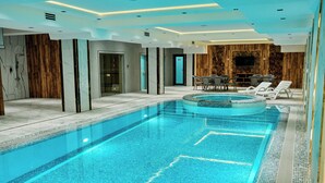 A modern indoor swimming pool with clear water, surrounded by lounge chairs and a wooden wall.