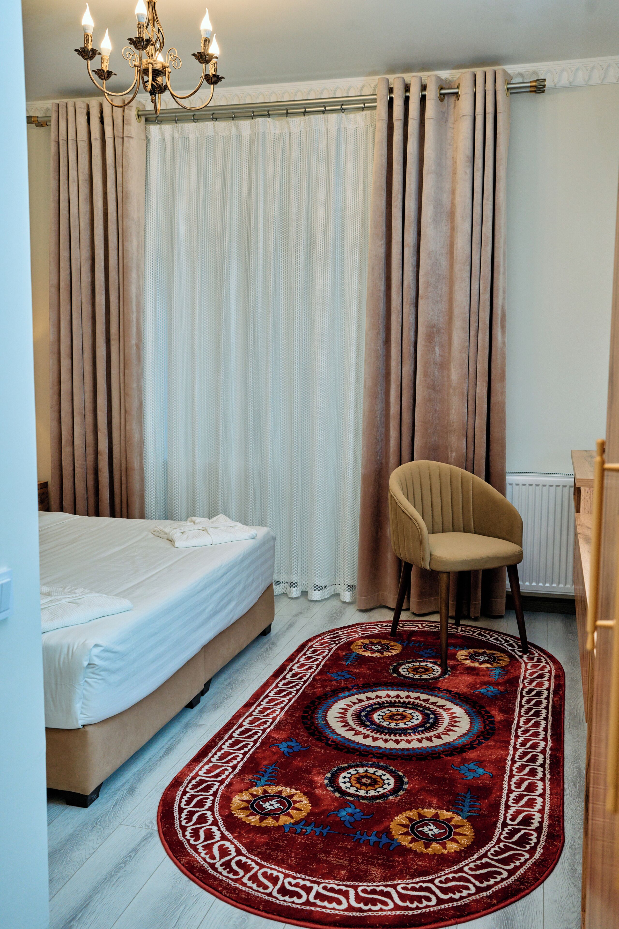 Un dormitorio con una cama, una silla, un tapete estampado y cortinas.