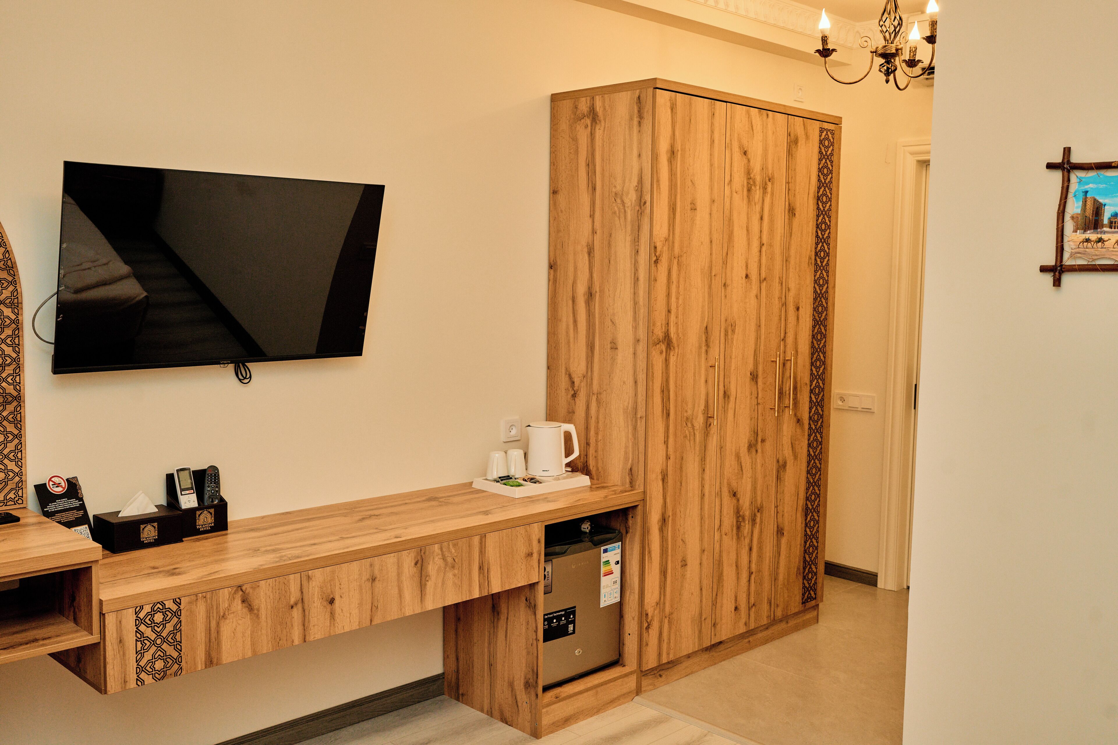 Quarto de hotel com secretária de madeira, televisão de tela plana na parede, cafeteira e minibar.