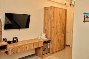 Habitación de hotel con un escritorio de madera, un televisor de pantalla plana montado en la pared, una cafetera y un minibar.