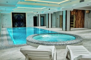 A modern indoor swimming pool with a hot tub, lounge chairs, and a wooden wall. - ISKANDAR Hotel (Samarkand)
