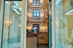 A hotel lobby with a checkered floor, a bed with ornate headboard, and a balcony with multiple windows. - ISKANDAR Hotel (Samarkand)