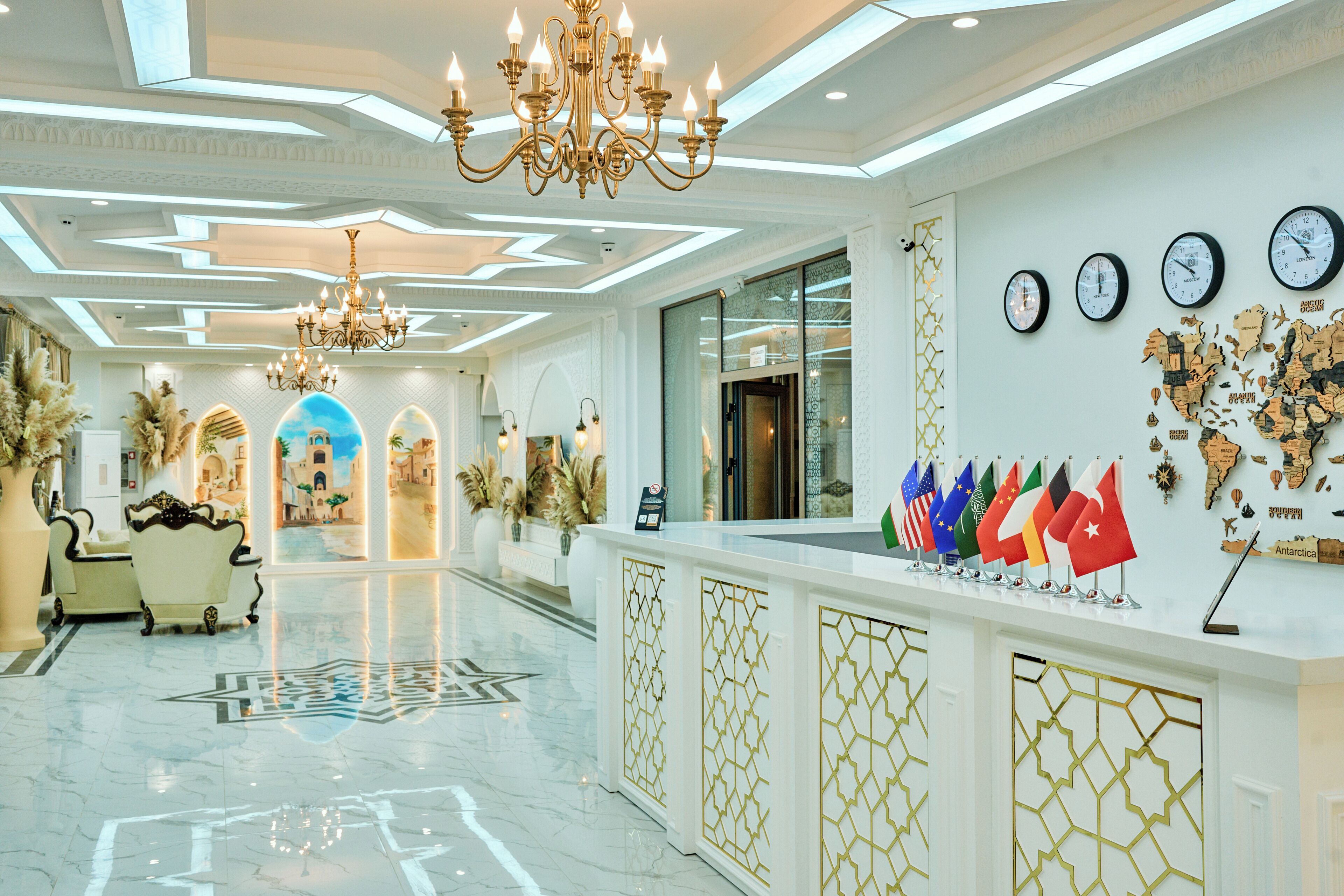Um hall de hotel com um candelabro, uma mesa de recepção e uma parede com relógios e bandeiras.