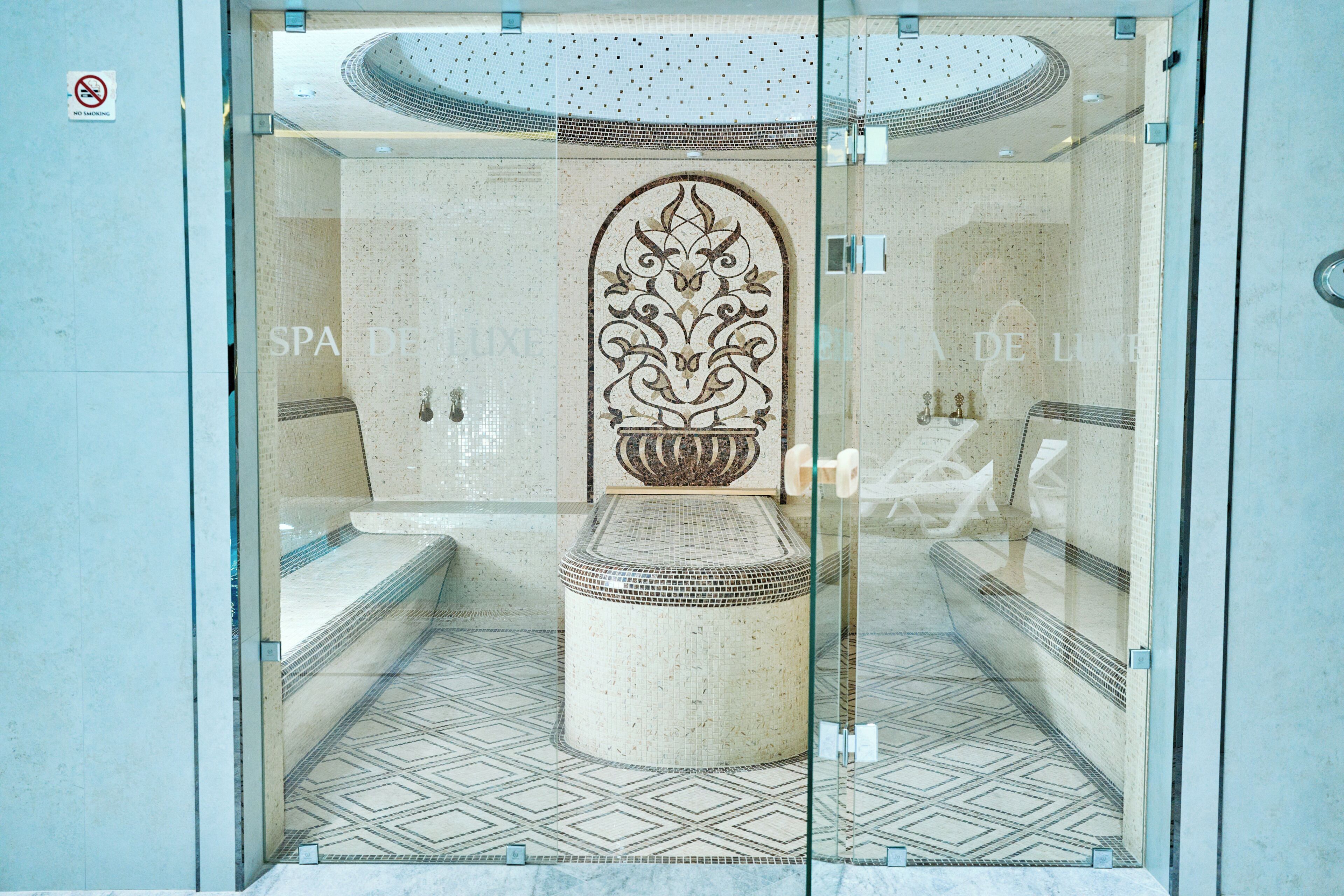 Um espaço de spa com piso azulejado, uma coluna decorativa central e um painel de vidro.