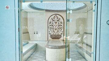 Um espaço de spa com piso azulejado, uma coluna decorativa central e um painel de vidro.