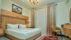 A hotel room with a large bed, a desk, a chair, and a patterned rug.
