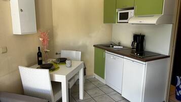 A compact kitchen with a microwave, coffee maker, and a small dining area with a chair and table.