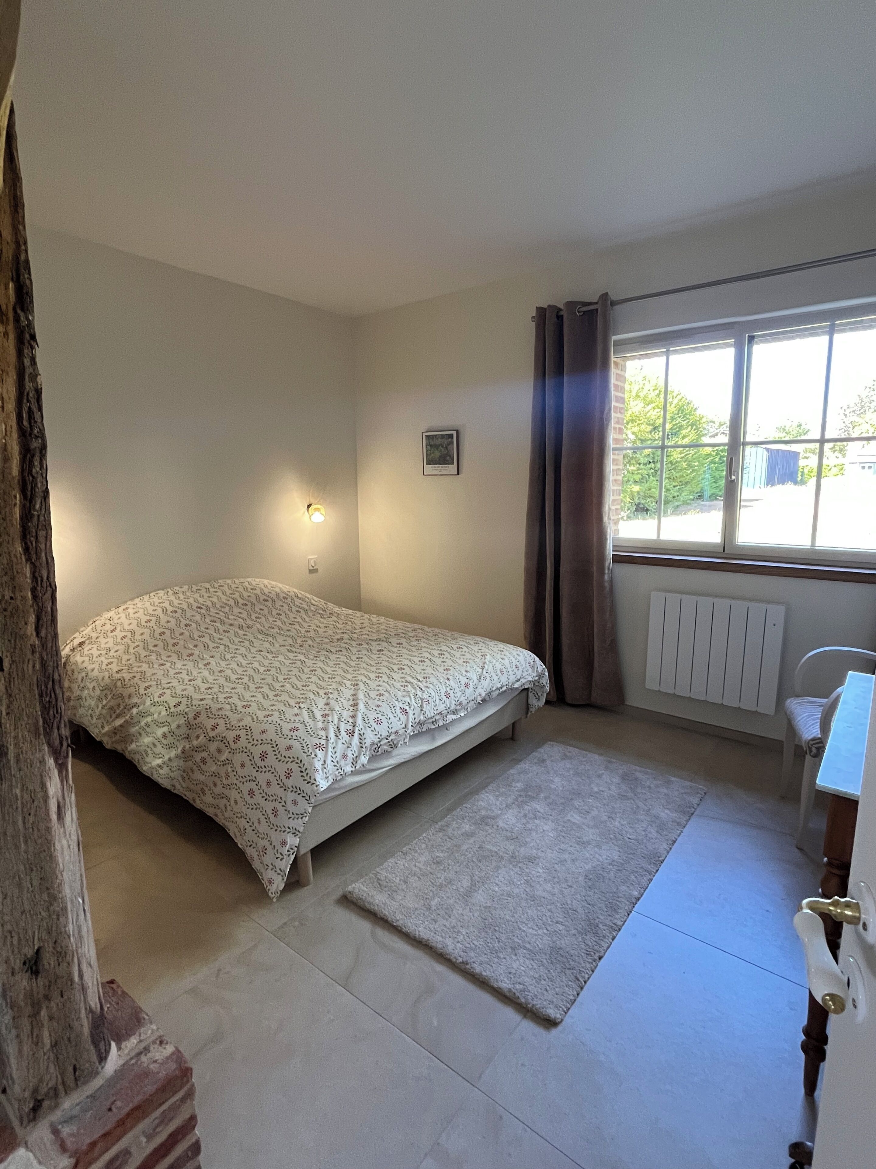 A bedroom with a bed, a radiator, a window with curtains, and a small table.