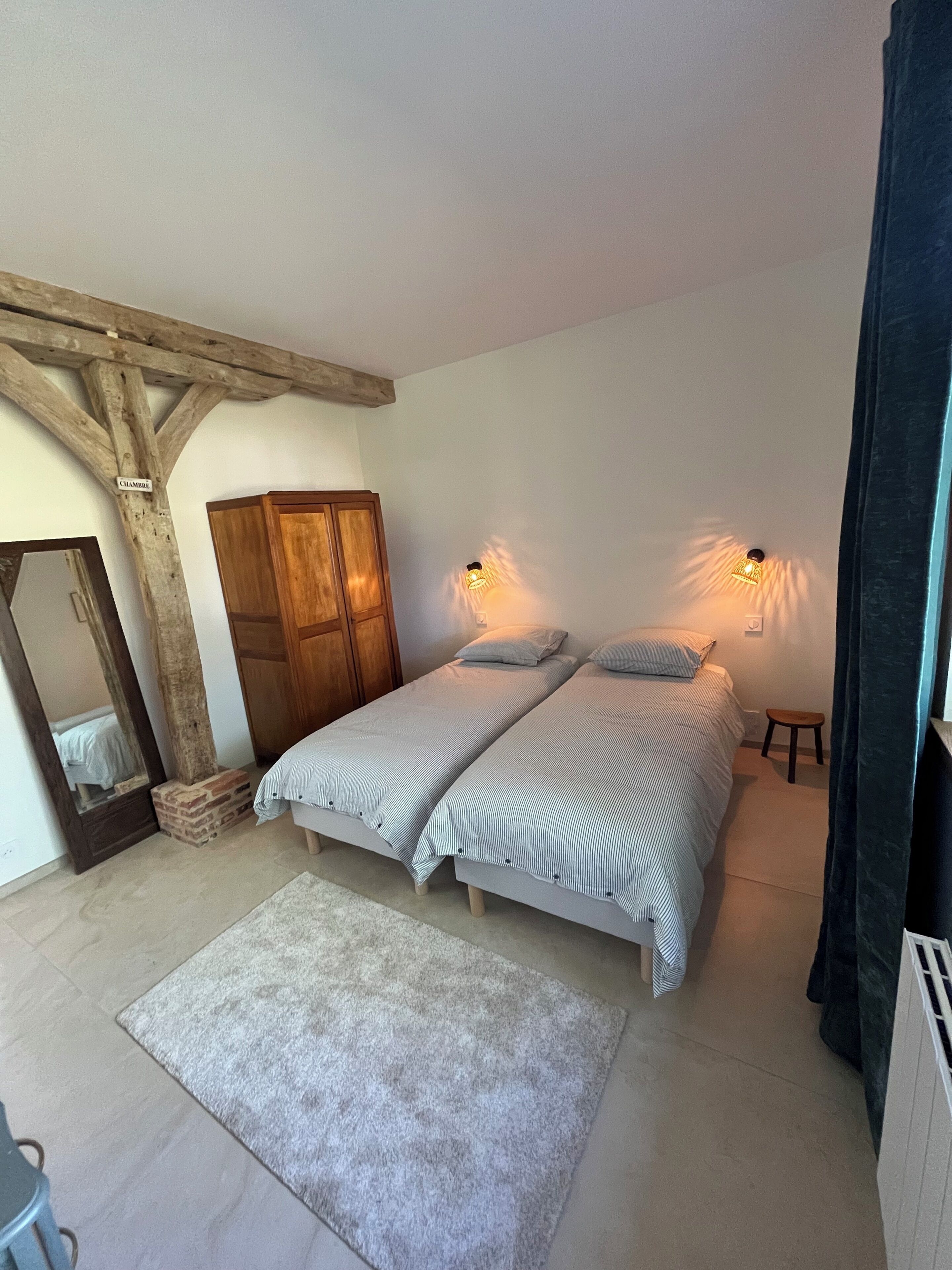 A bedroom with a double bed, a wooden wardrobe, a mirror, and two wall-mounted lights.