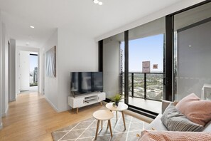 Un salon moderne doté d’un téléviseur à écran plat, d’un canapé, d’une petite table et d’un balcon offrant une vue sur la ville.