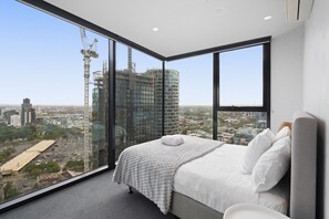 Ein modernes Schlafzimmer mit einem großen Bett, Blick auf die Stadt und einem Hochhaus im Hintergrund.