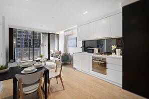 Una cocina moderna con armarios blancos, un comedor con mesa negra y una sala de estar con sofá.