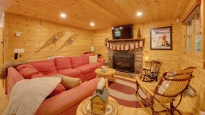 A cozy log cabin interior with a fireplace, a television mounted above it, and a red sofa. - North Conway: Updated 3BR Cabin Sleeps 9, Fire Pit (North Conway)