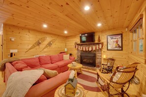 Ein gemütliches Blockhaus-Interieur mit Kamin, einem darüber montierten Fernseher und einem roten Sofa.