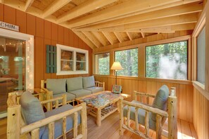 A cozy cabin interior with a wooden floor, a sofa, a table with a puzzle, and a window with a view of trees.