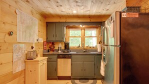 A compact kitchen with wooden cabinets, a built-in dishwasher, and a refrigerator. - North Conway: Updated 3BR Cabin Sleeps 9, Fire Pit (North Conway)