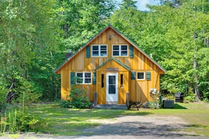 Une cabane en bois portant l’inscription « Cabane familiale », avec une porte d’entrée, des fenêtres et un petit espace porche.