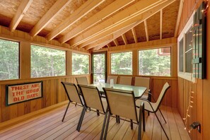 A wooden interior with a dining table and chairs, large windows, and a sign on the wall.