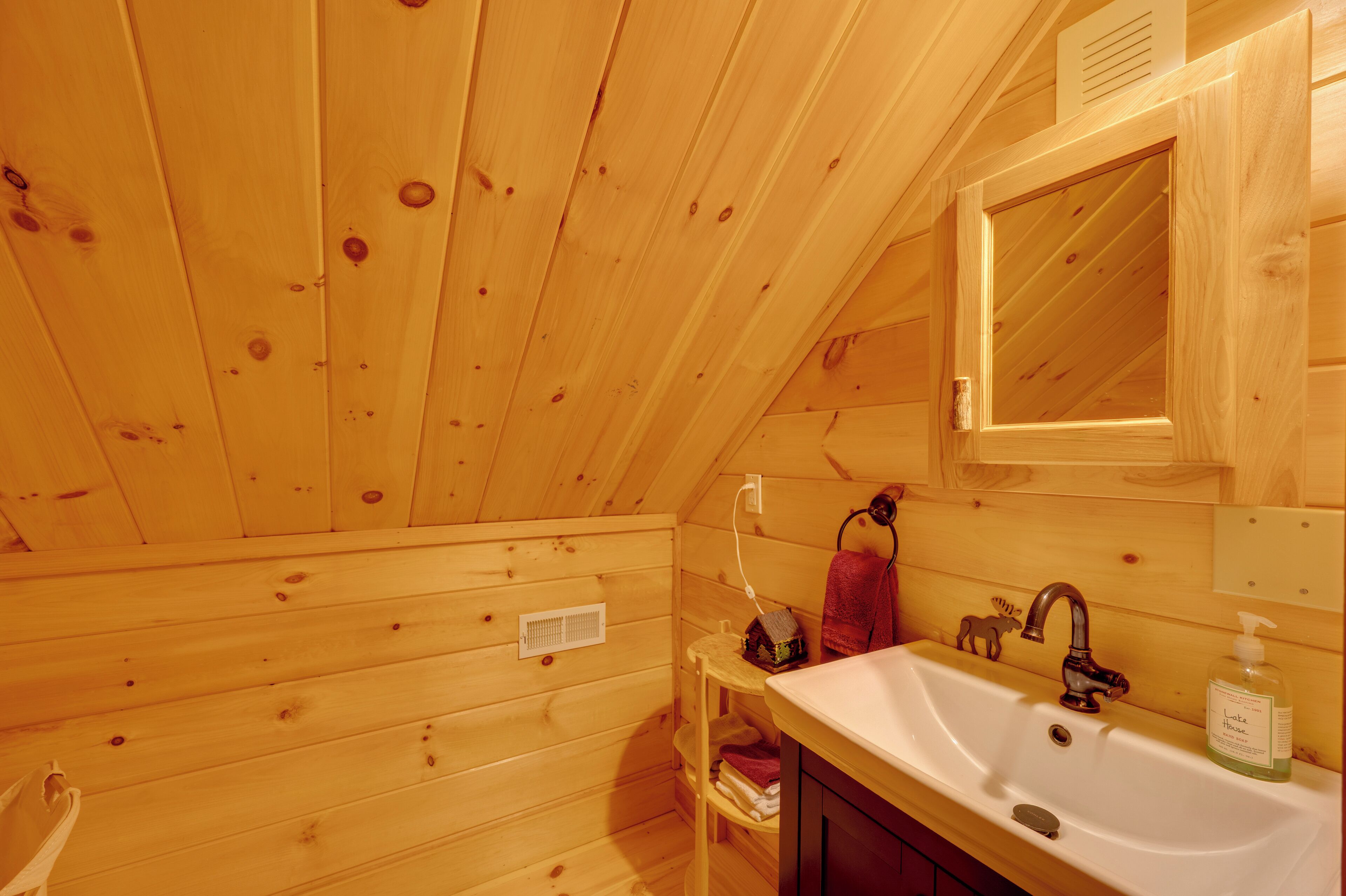 A wooden cabin bathroom with a sink, mirror, and towel rack.