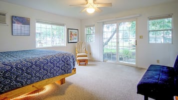 A bedroom with a bed, a chair, a ceiling fan, and large windows.