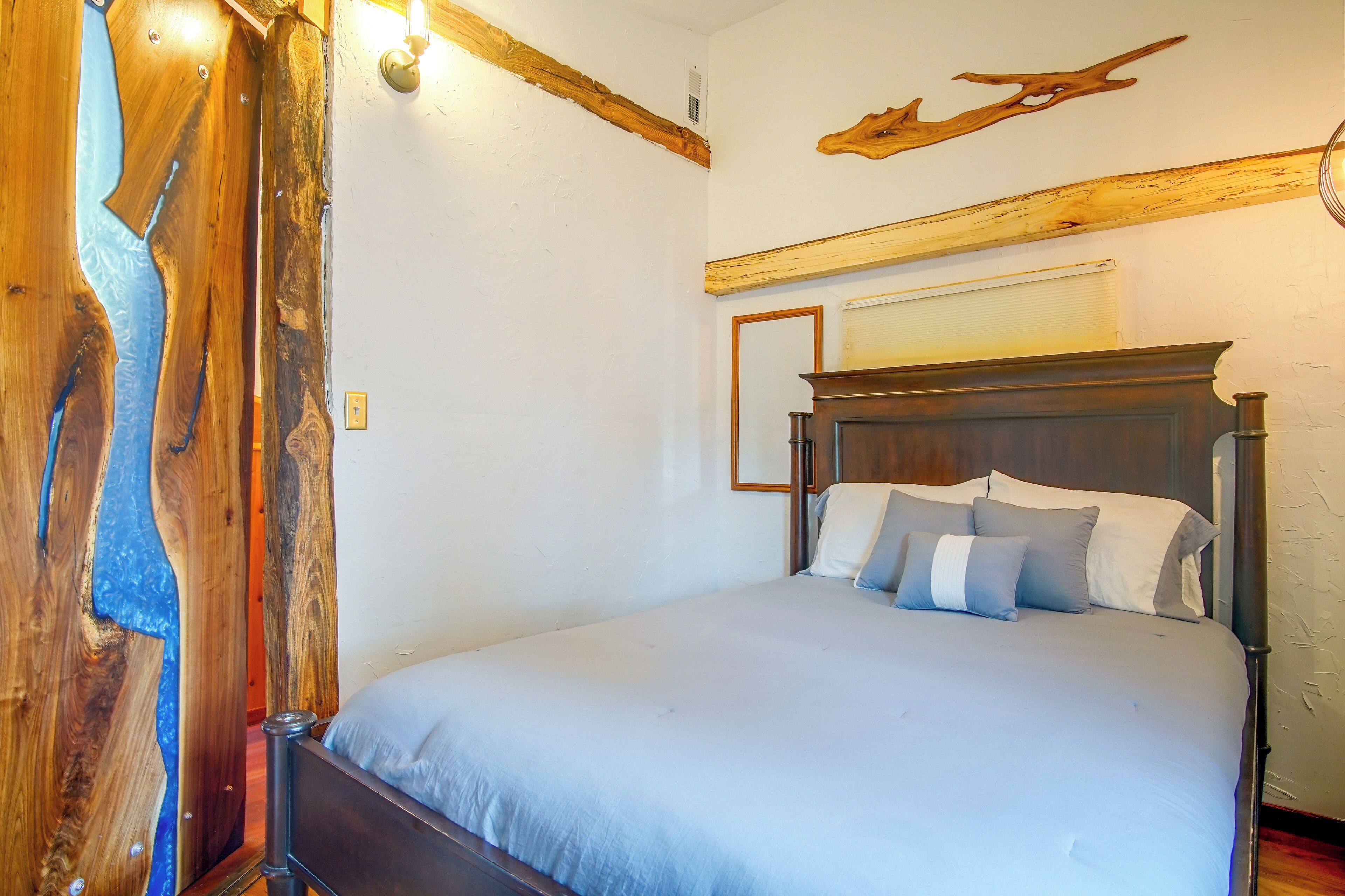 A bedroom with a wooden headboard, a bed with grey bedding, and a wooden wall accent.