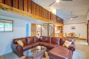 A spacious living room with a brown leather sectional sofa, a glass coffee table, and a wooden staircase leading to an upper level.