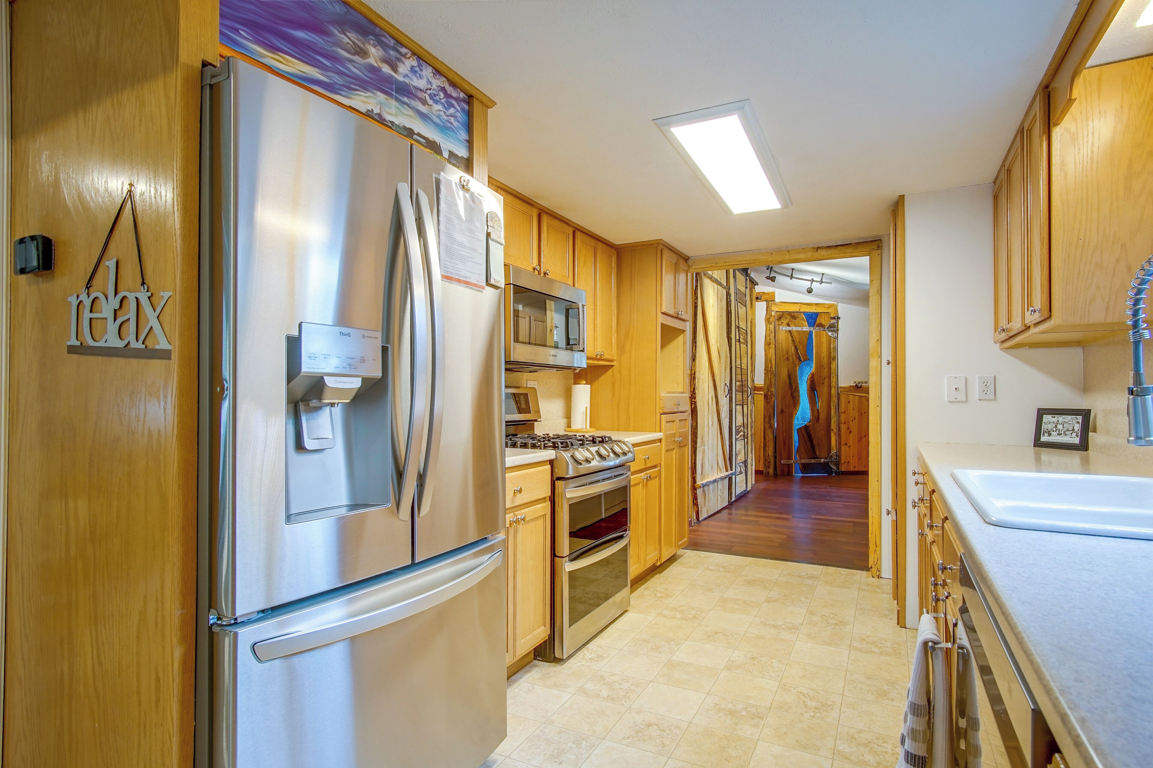 A modern kitchen with stainless steel appliances, wooden cabinets, and a visible hallway leading to another room.
