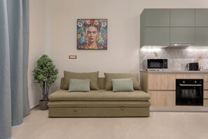 Un saló modern amb un sofà, una planta en test i una cuina amb microones i forn.