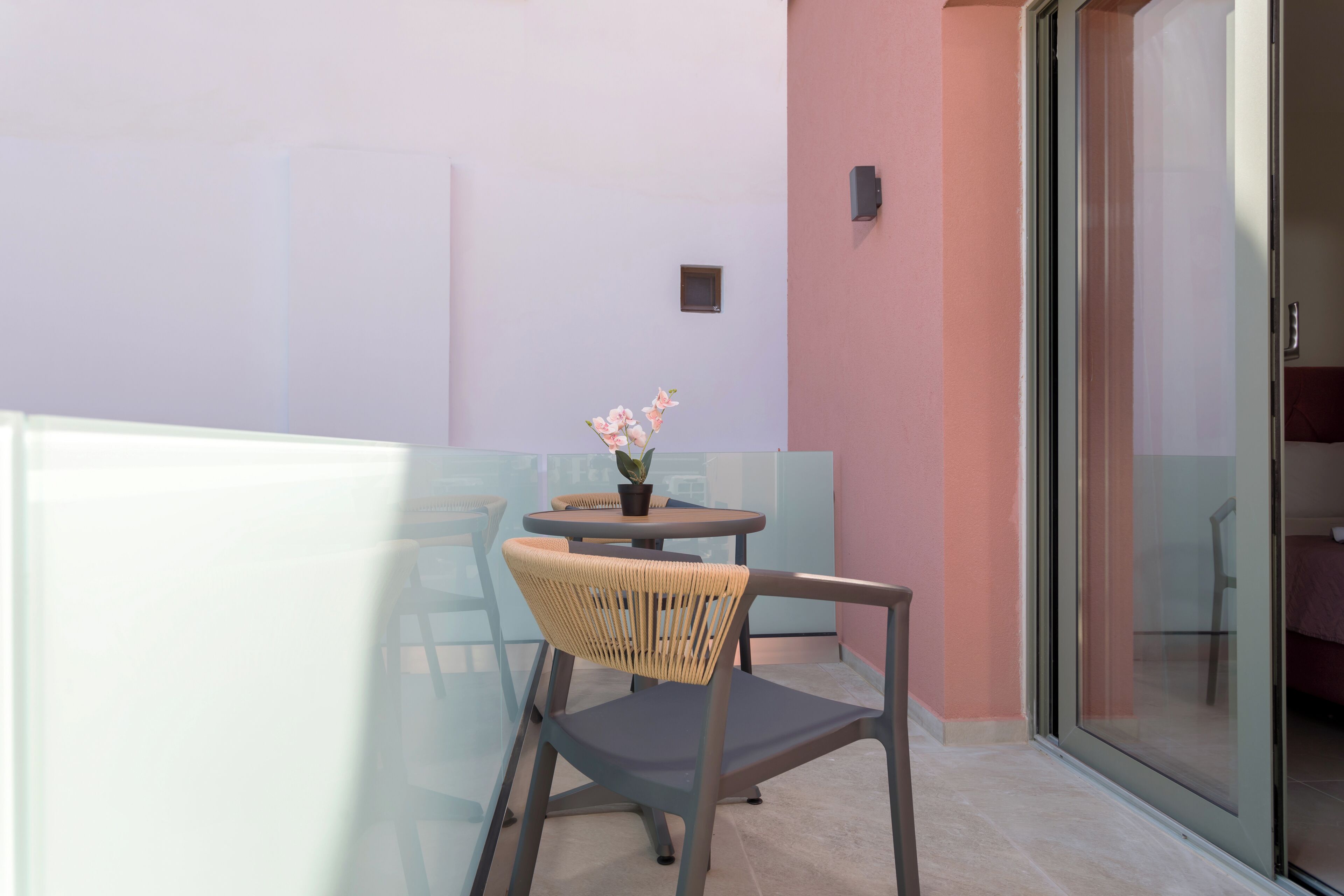 A balcony with a table and chairs, a potted plant, and a sliding glass door leading to an interior space.