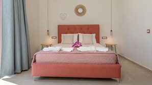 Un letto rifatto con lenzuola bianche e una coperta rosa, due comodini, un portalampada a parete e uno specchio decorativo.