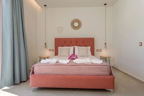 Ein ordentlich bezogenes Bett mit weißen Laken und einer rosa Tagesdecke, zwei Nachttische, eine Wandleuchte und ein dekorativer Spiegel.