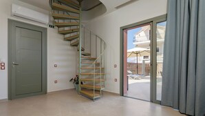 Una scala a chiocciola con gradini in legno e ringhiere in metallo, che conduce a un balcone con vista su posti a sedere all'aperto e un edificio.