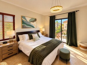 A hotel room with a bed, bedside tables, a lamp, a painting, a balcony with curtains, and a view of the outside. - Stylish 3BR villa in Gold Coast Aruba with private pool, gym, tennis courts and gated resort amenities. (Noord)