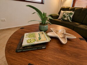 A round wooden table with a book titled 'Gardens for Science & Pleasure' and a starfish decoration. - Stylish 3BR villa in Gold Coast Aruba with private pool, gym, tennis courts and gated resort amenities. (Noord)
