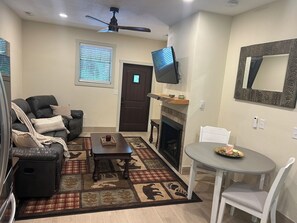 Una sala de estar con chimenea, televisor montado arriba, ventilador de techo y comedor con mesa y sillas.