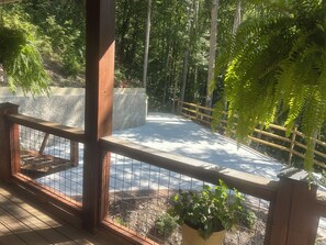 Una terraza de madera con barandilla metálica, rodeada de follaje y un muro de piedra.