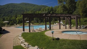 A pool area with a pergola, lounge chairs, and a view of a forested hill. - Beautiful getaway at “Maggie Valley Resort” (Maggie Valley)