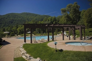 A pool area with a pergola, lounge chairs, and a view of a forested hill. - Beautiful getaway at “Maggie Valley Resort” (Maggie Valley)