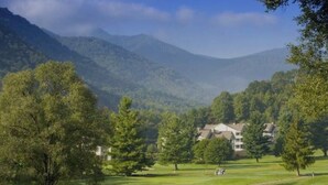 A golf course with a clubhouse and trees in the foreground, and mountains in the background. - Beautiful getaway at “Maggie Valley Resort” (Maggie Valley)