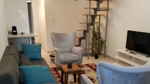 A modern living room with a sofa, armchairs, a coffee table, a TV, and a staircase. - Comfortable and well-equipped accommodations (Ville-la-Grand)