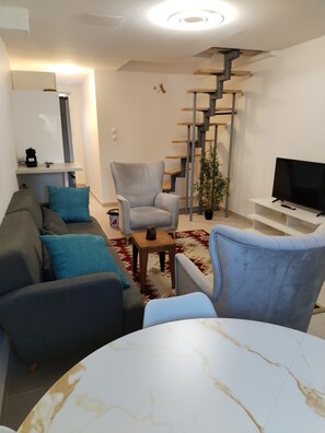 Ein modernes Wohnzimmer mit einer Couch, Sesseln, einem Couchtisch, einem Fernseher und einer Treppe.