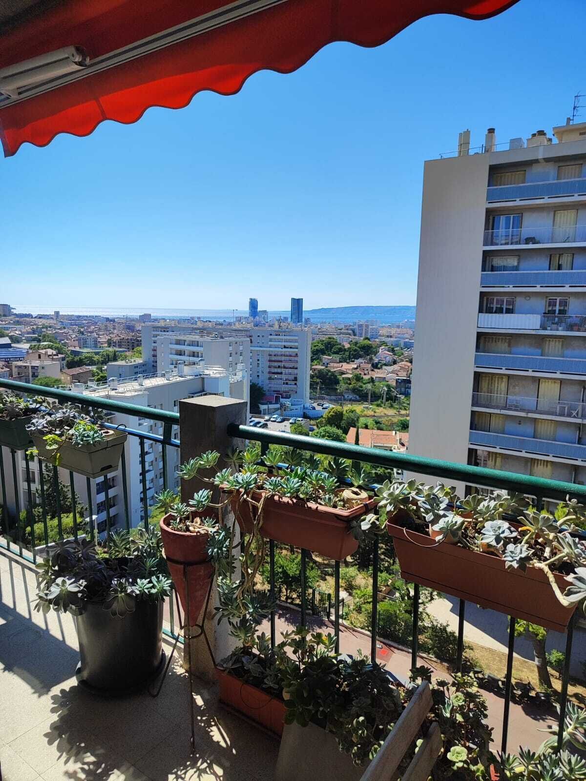 Un balcon agrémenté de plantes en pot, une vue sur le paysage urbain et un ciel bleu dégagé.